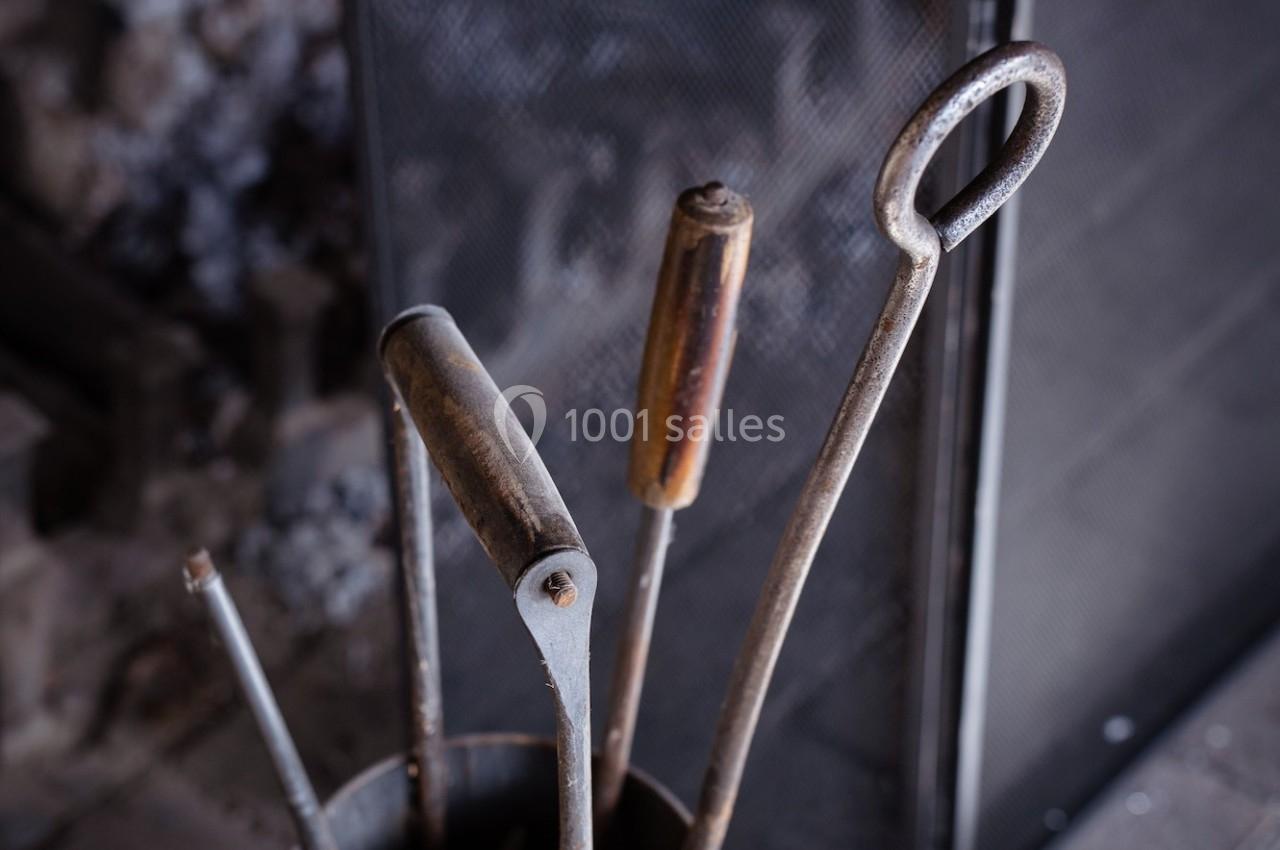 Outils en métal pour cheminée rangés dans un support cylindrique devant un pare-feu en métal.
