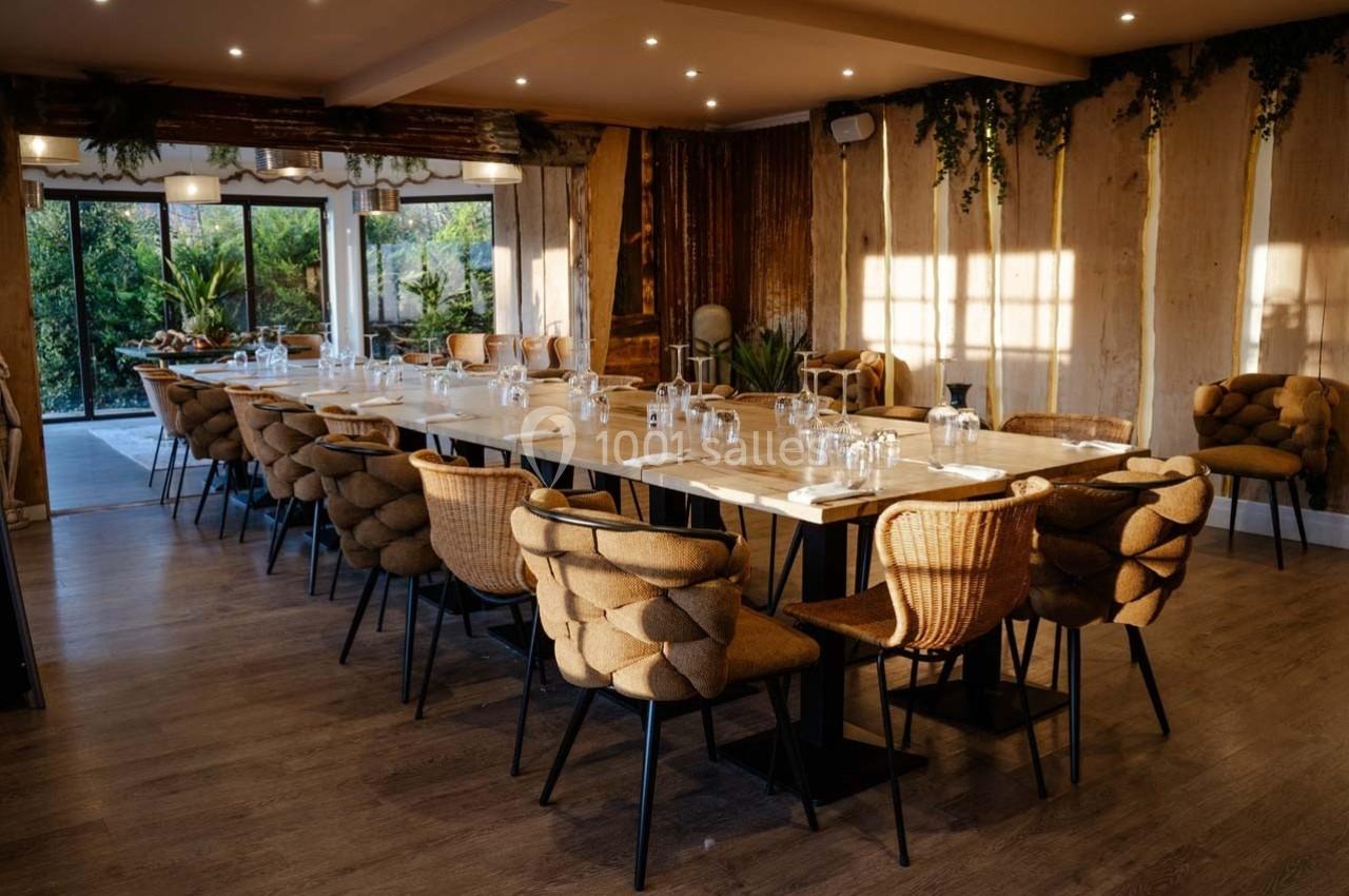 Salle à manger lumineuse avec une grande table en bois, des chaises en rotin et une vue sur un jardin verdoyant.