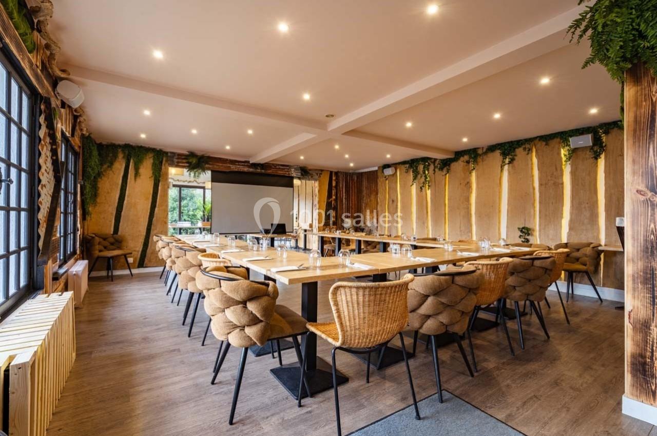 Salle de réunion lumineuse avec tables disposées en U, chaises en osier et décoration végétale sur les murs.