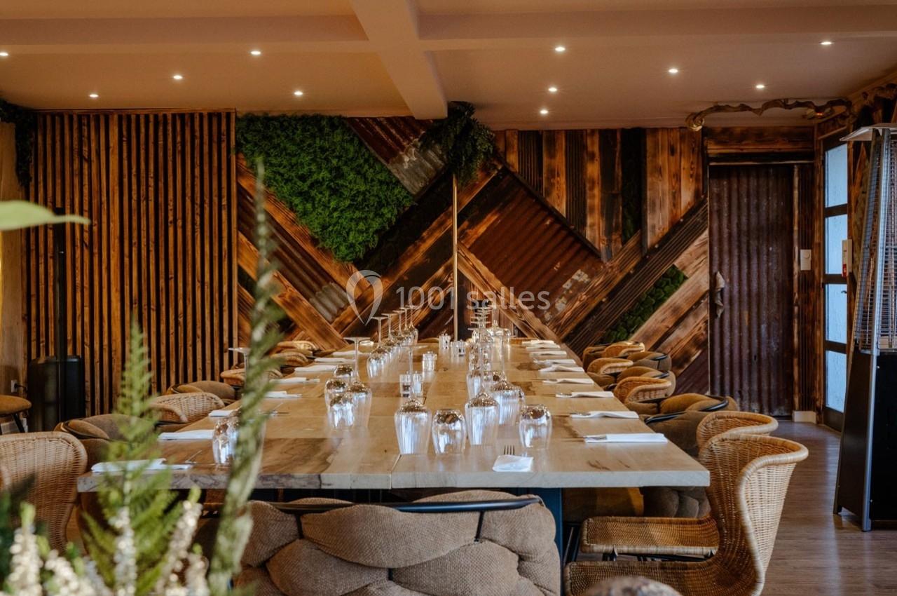 Salle à manger avec une grande table en bois, chaises en rotin et décoration murale en bois et végétation.