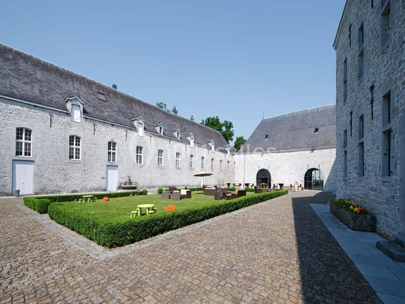 Cour intérieure pavée entourée de bâtiments en pierre, avec des tables et chaises installées sur une pelouse centrale.