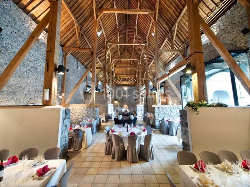 Salle de réception avec murs en pierre, poutres apparentes et tables dressées pour un événement.