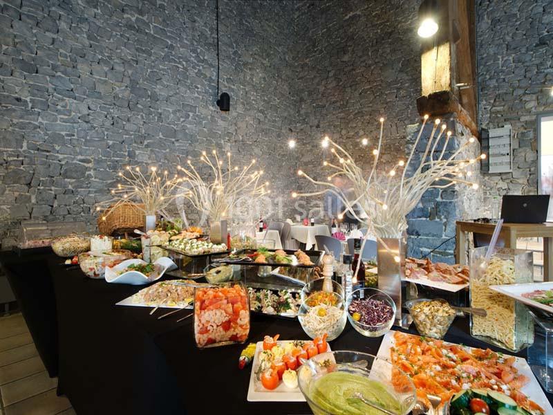 Buffet varié avec plats froids et chauds, présenté dans une salle en pierre avec décorations lumineuses.