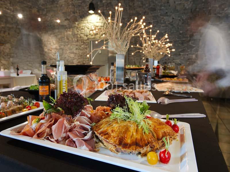 Plateau de charcuterie et pâté en croûte décoré de légumes, disposé sur une table de buffet dans une salle en pierre.