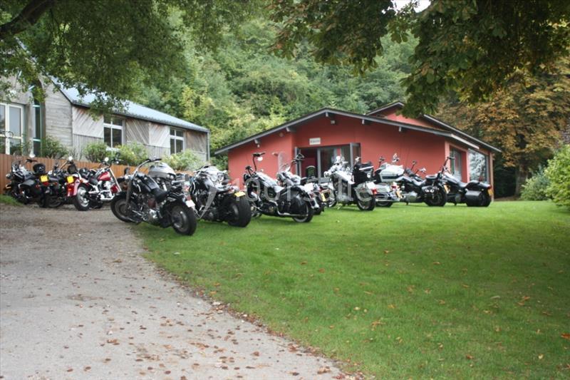 Plusieurs motos stationnées devant un bâtiment rouge entouré de verdure.