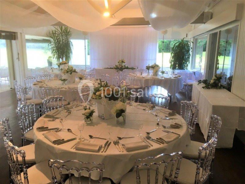 Salle de réception décorée avec des tables rondes dressées, nappes blanches et compositions florales.
