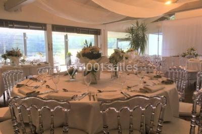 Salle de réception décorée pour un mariage, avec des tables rondes dressées, nappes blanches et arrangements floraux.