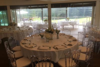 Salle de réception décorée pour un mariage, avec des tables rondes dressées, nappes blanches et arrangements floraux.