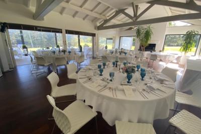 Salle de réception décorée pour un mariage, avec des tables rondes dressées, nappes blanches et arrangements floraux.