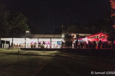 Salle de réception décorée pour un mariage, avec des tables rondes dressées, nappes blanches et arrangements floraux.