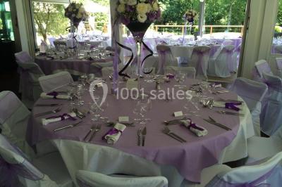 Salle de réception décorée pour un mariage, avec des tables rondes dressées, nappes blanches et arrangements floraux.