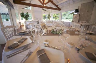 Salle de réception décorée pour un mariage, avec des tables rondes dressées, nappes blanches et arrangements floraux.