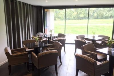 Salle lumineuse avec baies vitrées, tables rondes dressées avec nappes blanches et chaises modernes.