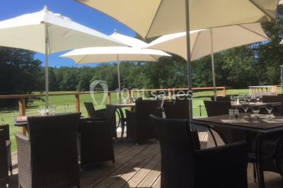 Salle lumineuse avec baies vitrées, tables rondes dressées avec nappes blanches et chaises modernes.
