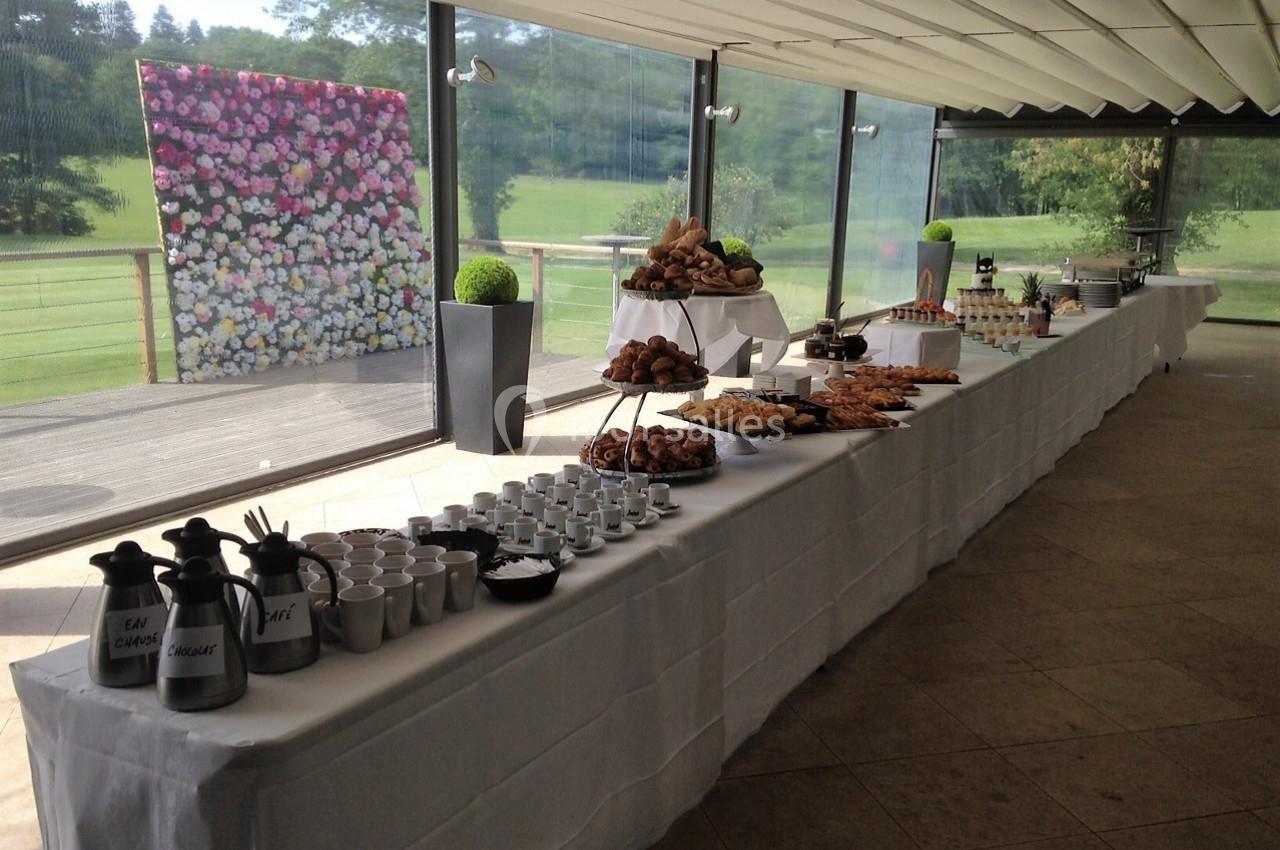 Buffet dressé dans une salle lumineuse avec vue sur un jardin, comprenant viennoiseries, boissons et décor floral.