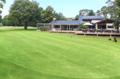 Salle lumineuse avec baies vitrées, tables rondes dressées avec nappes blanches et chaises modernes.