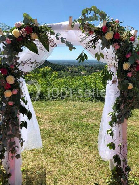 Arche de mariage décorée de fleurs et de voilages blancs, avec vue sur un paysage verdoyant en arrière-plan.