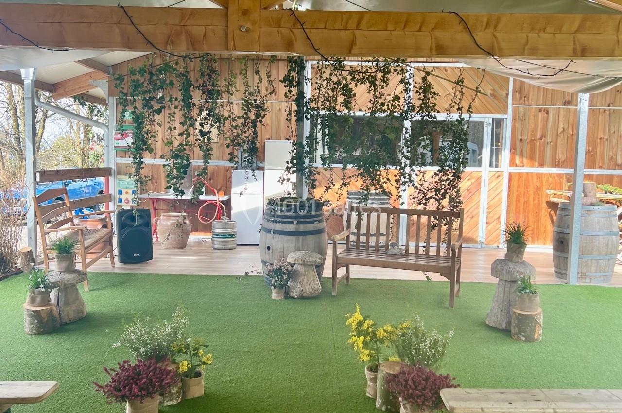 Espace extérieur couvert avec toit en bois, bancs, plantes décoratives et sol en gazon synthétique.