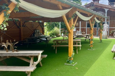 Salle en bois avec des bancs alignés sur un sol en gazon synthétique, décorée de fleurs suspendues.