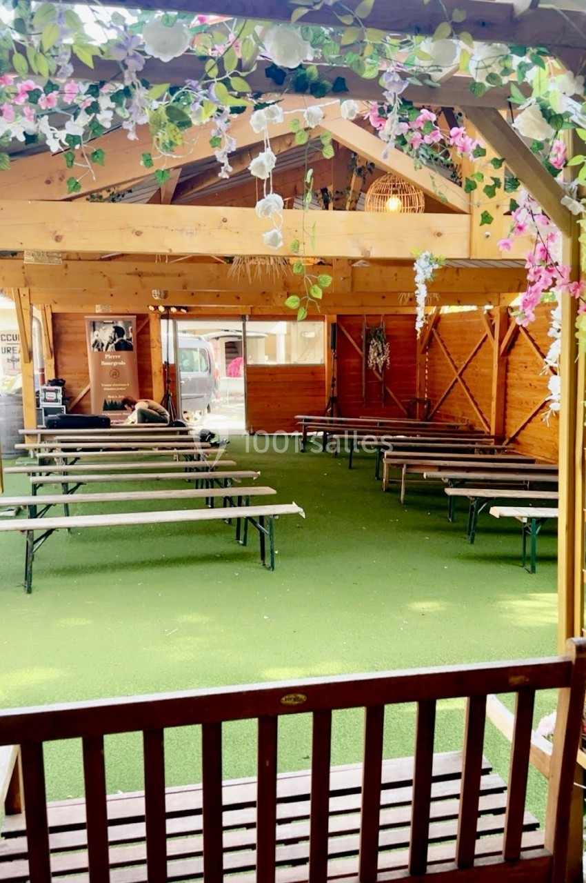 Salle en bois avec des bancs alignés sur un sol en gazon synthétique, décorée de fleurs suspendues.
