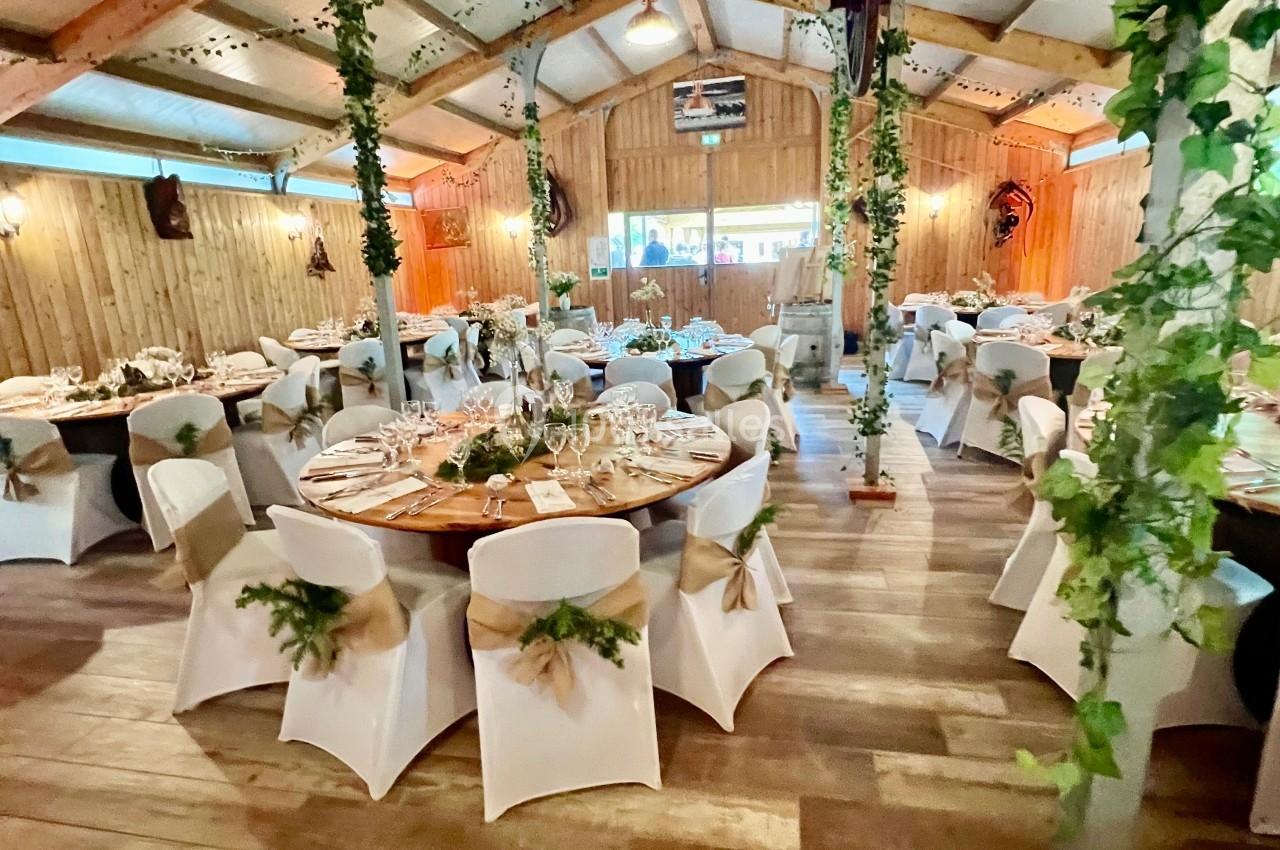 Salle de réception décorée avec des tables rondes, nappes blanches, chaises habillées et guirlandes végétales suspendues.