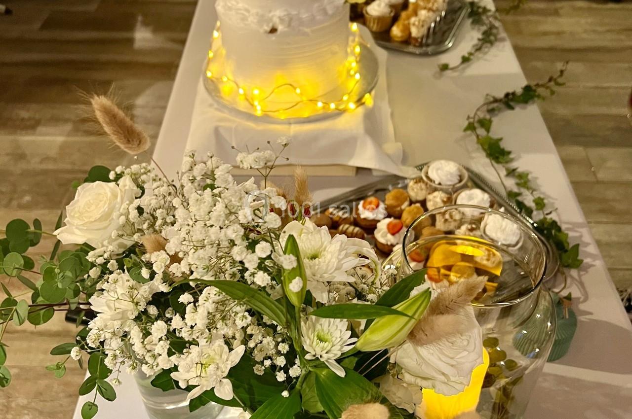 Table décorée pour un mariage avec un gâteau blanc à étages, fleurs blanches et un assortiment de desserts.