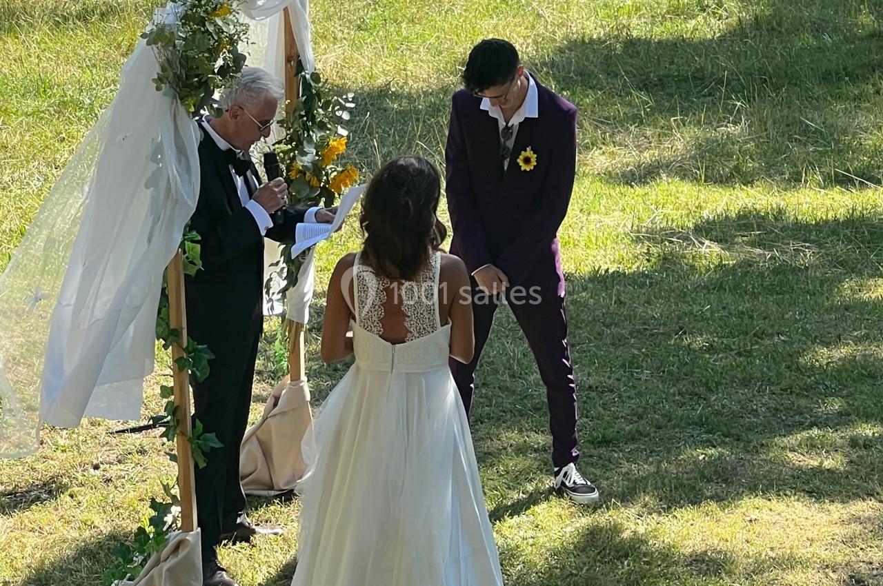Un couple se tient devant un officiant lors d'une cérémonie de mariage en plein air, entouré de verdure.