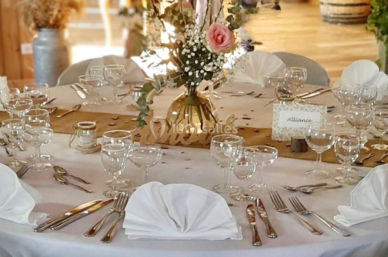 Table ronde décorée pour un événement, avec nappes blanches, vaisselle élégante et centre de table floral.