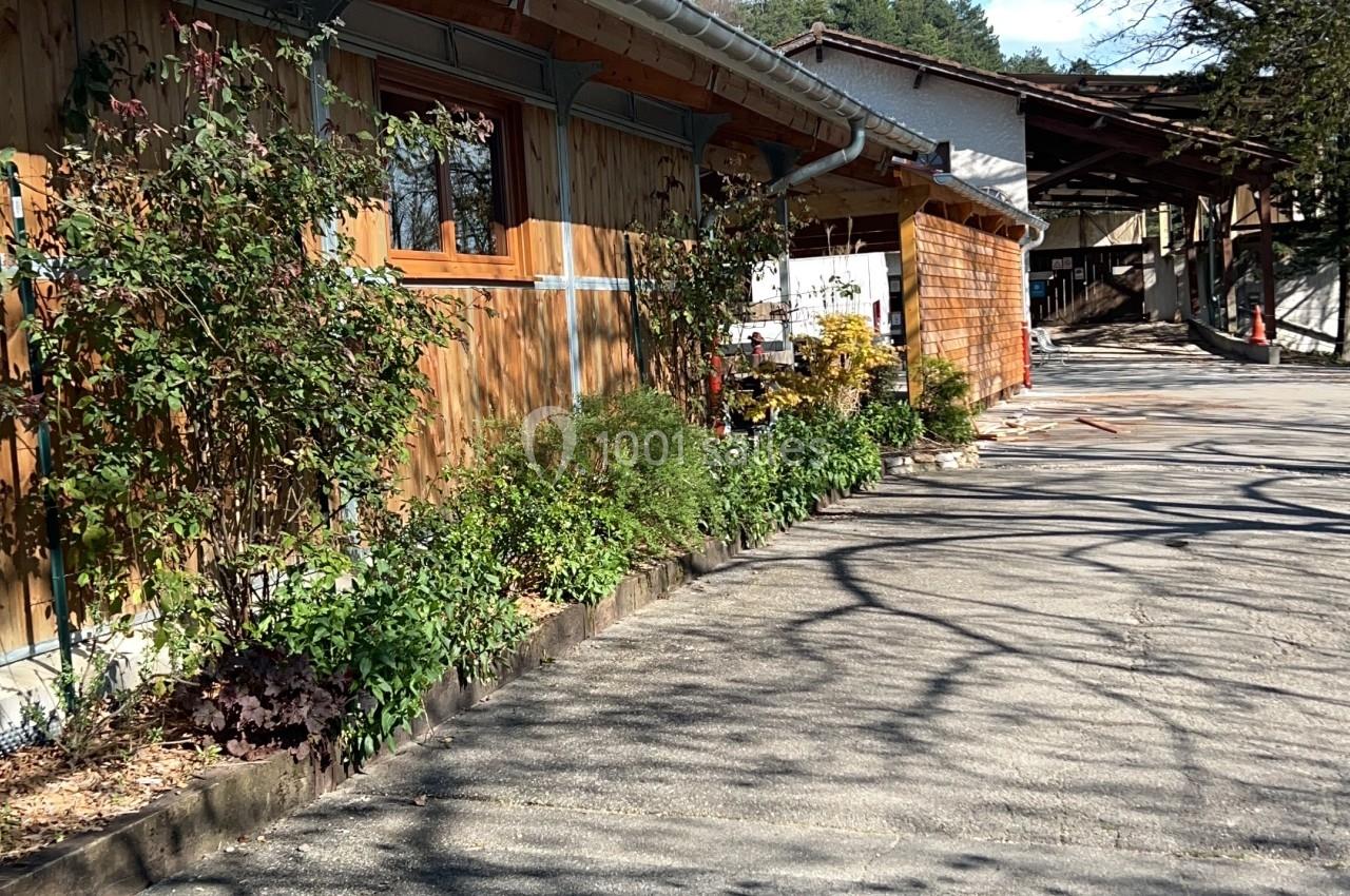Allée bordée de bâtiments en bois et de végétation, sous un ciel bleu dégagé.