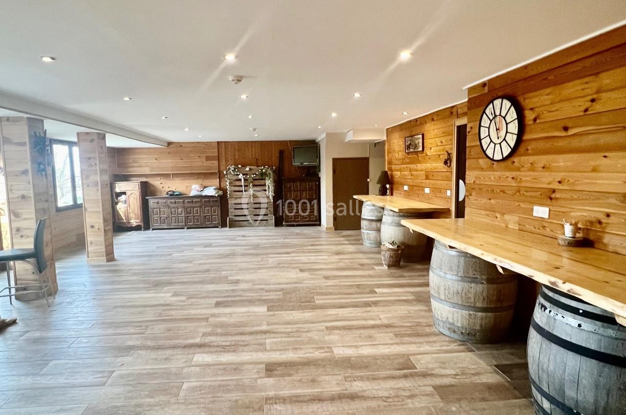 Salle spacieuse avec sol en bois clair, murs en bois, bar en arrière-plan et tonneaux décoratifs.