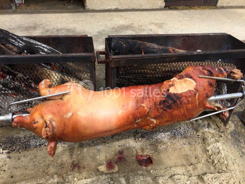 Cochon entier rôti à la broche au-dessus de braises dans un cadre extérieur.
