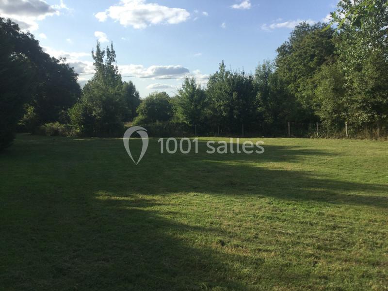 Pelouse verdoyante entourée d'arbres sous un ciel bleu parsemé de quelques nuages.