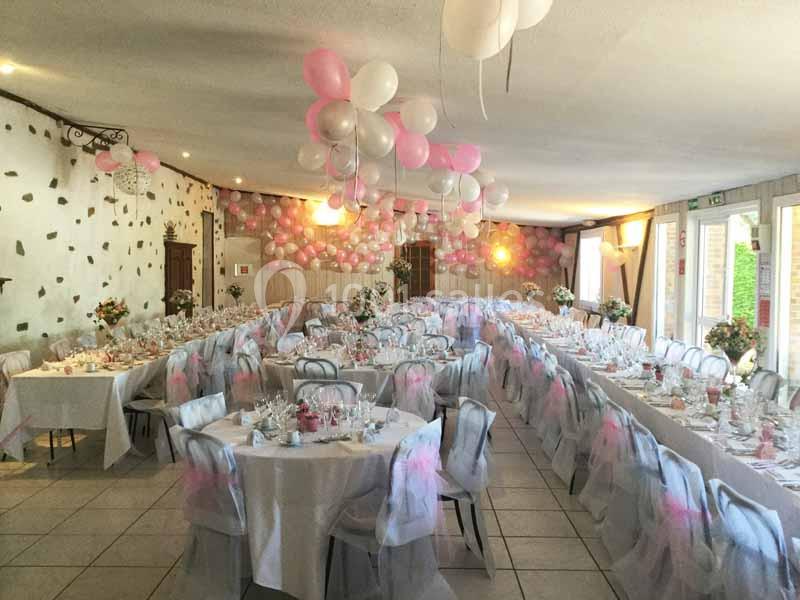 Salle de réception décorée avec des ballons roses et blancs, tables dressées pour un événement festif.