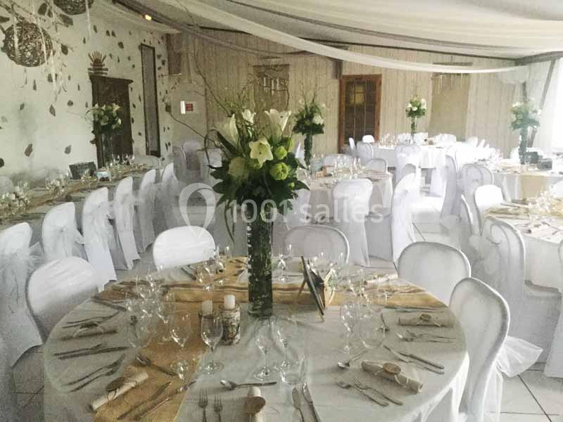 Salle de réception décorée avec des tables rondes dressées, nappes blanches et compositions florales au centre.