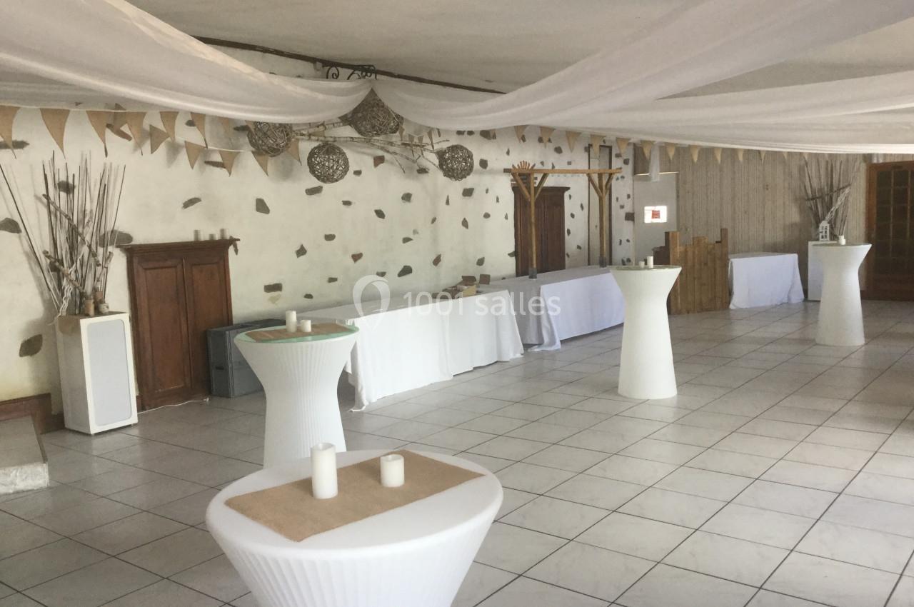 Salle décorée avec des tables hautes blanches, des nappes et des éléments suspendus dans un style épuré et chaleureux.