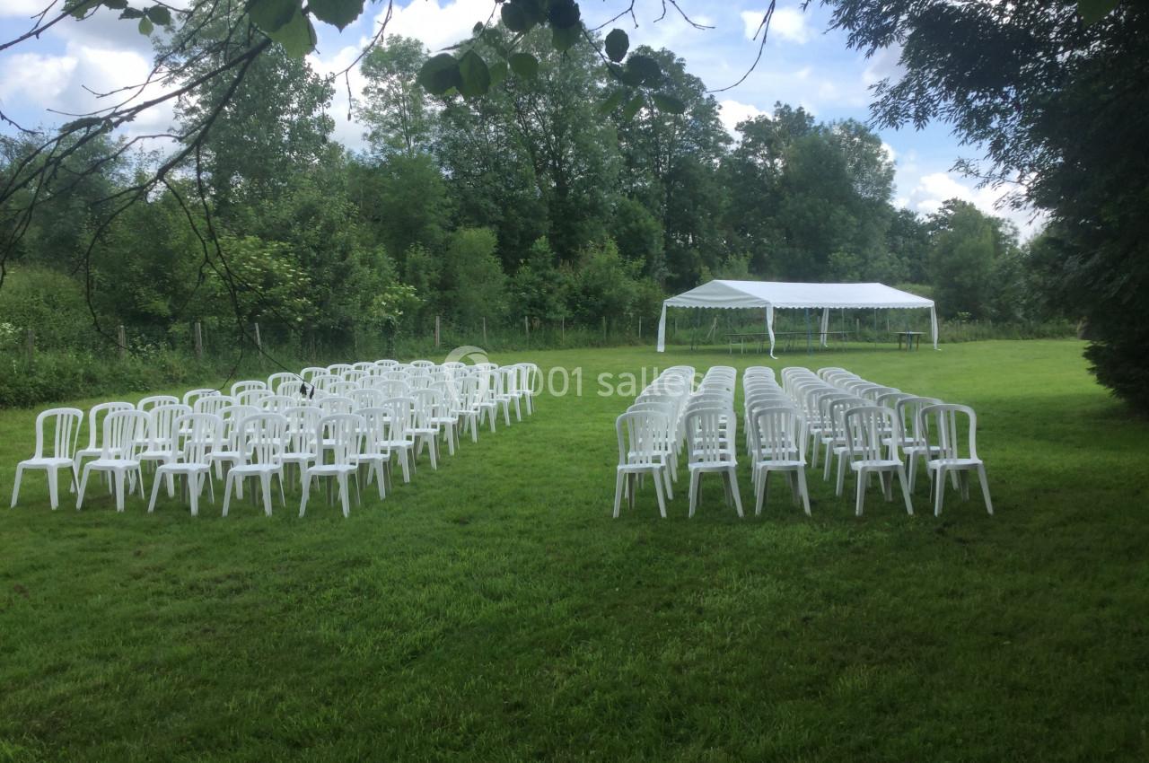 Chaises blanches alignées en extérieur sur une pelouse, avec une tente blanche au fond près d'arbres.