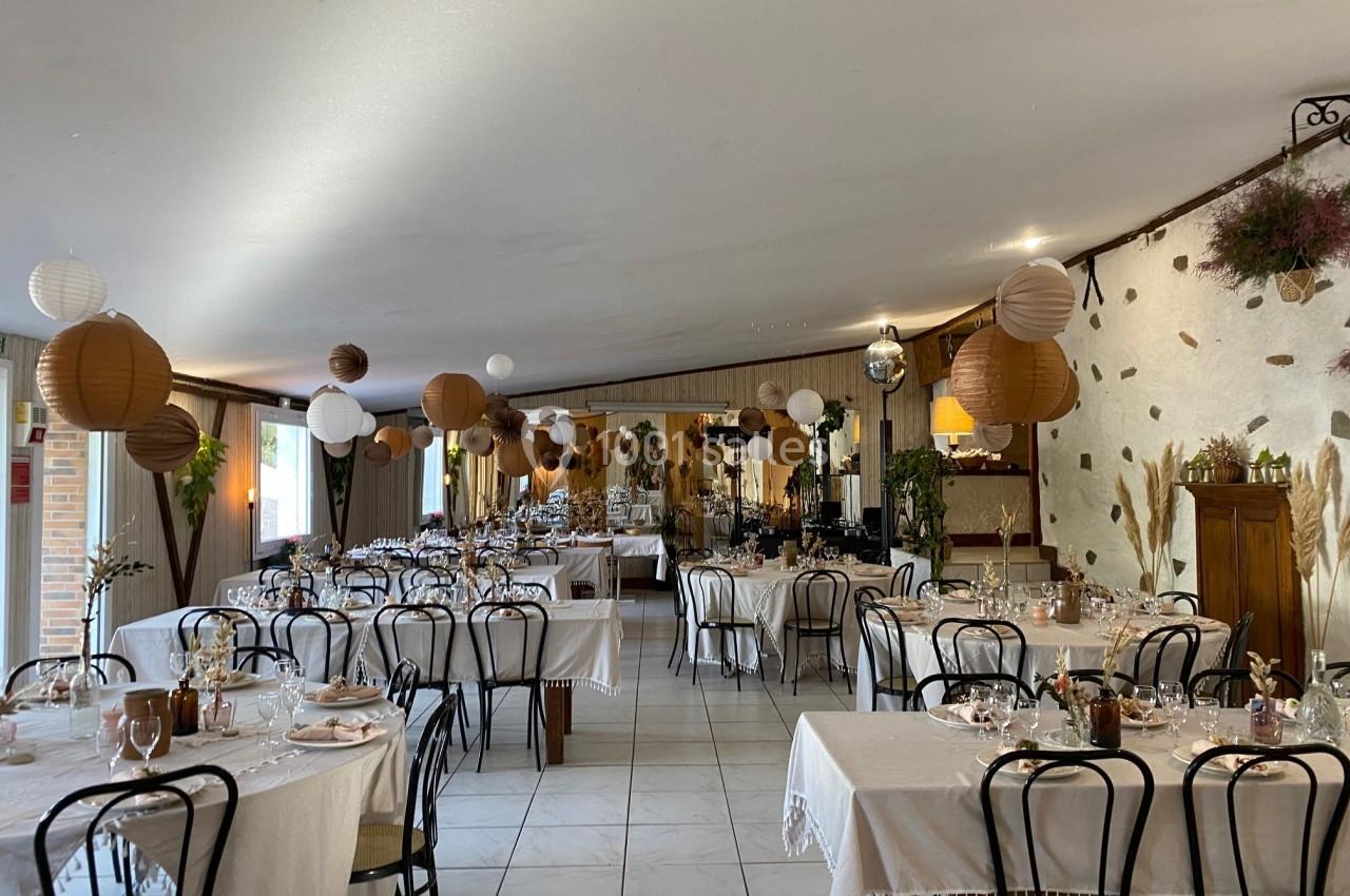 Salle de réception décorée avec des tables dressées, des lanternes suspendues et une ambiance chaleureuse.