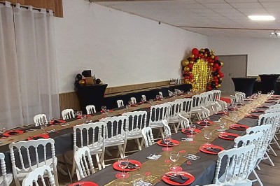 Décoration festive avec arche de ballons rouges, noirs et dorés, rideau scintillant et tapis rouge dans une salle.