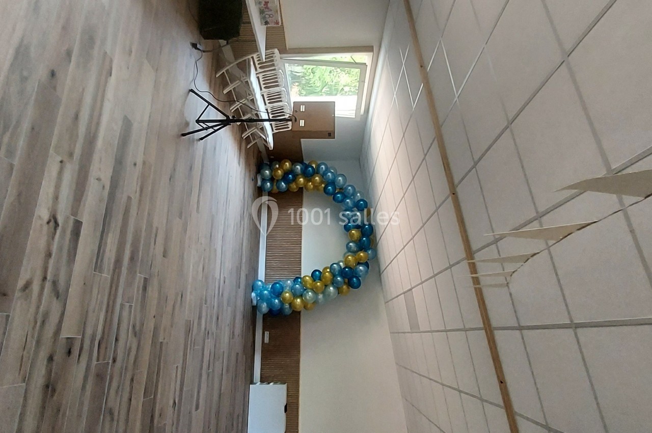 Guirlande de ballons bleus et jaunes décorant une salle lumineuse avec parquet et murs clairs.