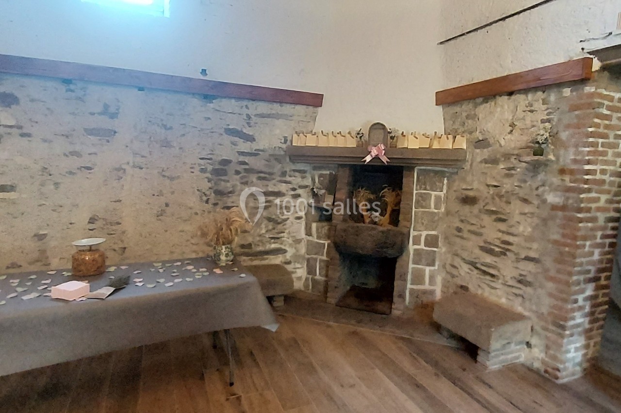 Salle rustique avec murs en pierre, cheminée décorée et table recouverte d'une nappe grise avec des objets disposés.