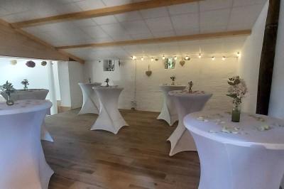 Salle de réception avec une table ronde décorée, des ballons et une grande table dressée en arrière-plan.