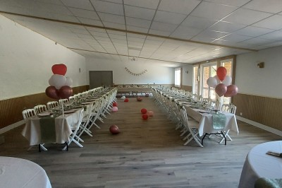 Salle de réception avec une table ronde décorée, des ballons et une grande table dressée en arrière-plan.