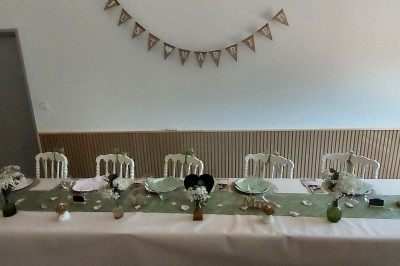 Salle de réception avec une table ronde décorée, des ballons et une grande table dressée en arrière-plan.