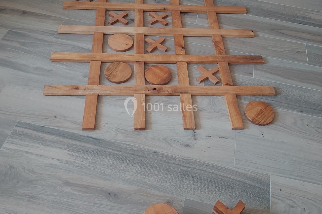 Jeu de morpion en bois avec des pièces rondes et en croix disposées sur un sol en parquet clair.