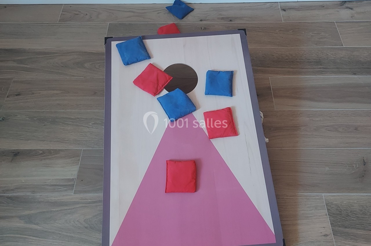 Planche de jeu de lancer avec des sacs en tissu rouges et bleus, posée sur un sol en bois.