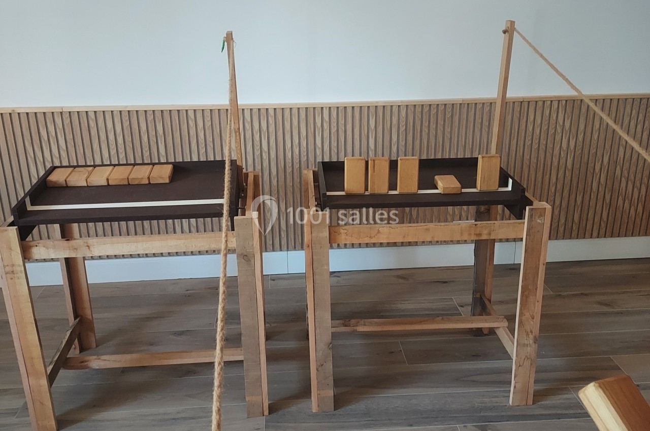 Deux tables en bois avec des blocs de bois alignés, reliées par une corde tendue, sur un sol en parquet.