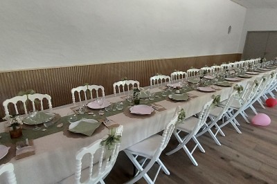 Salle de réception avec une table ronde décorée, des ballons et une grande table dressée en arrière-plan.