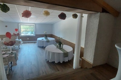 Salle de réception avec une table ronde décorée, des ballons et une grande table dressée en arrière-plan.