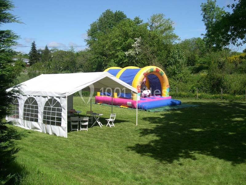 Structure gonflable colorée et tente blanche installées sur une pelouse dans un jardin verdoyant.
