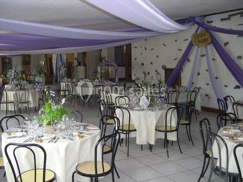 Salle de réception décorée avec des nappes blanches, des chaises noires et des drapés violets au plafond.